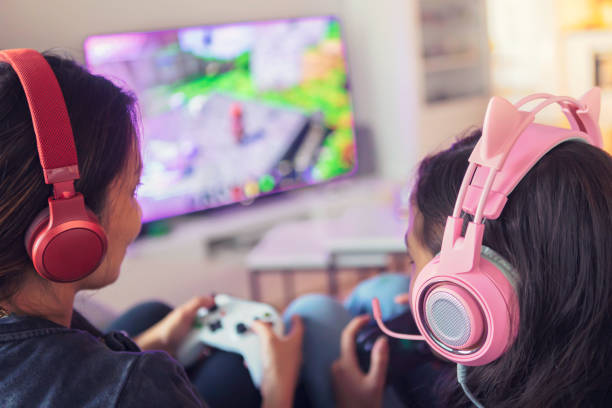Mother and daughter playing video games together Close up of a mother and daughter playing video games together on a video game console using gamepads and headsets. swedish girl stock pictures, royalty-free photos & images