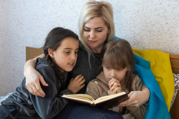 mother and daughter reading a book with the flag of ukraine in bed stock photo