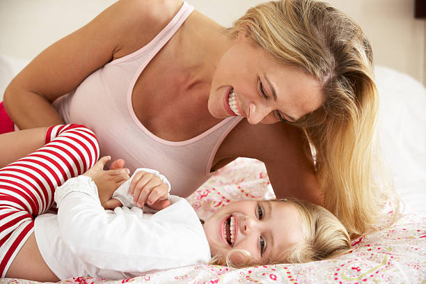 Mother And Daughter Relaxing Together In Bed Mother And Daughter Relaxing Together In Bed Having Fun Smiling tickling beautiful women pictures stock pictures, royalty-free photos & images