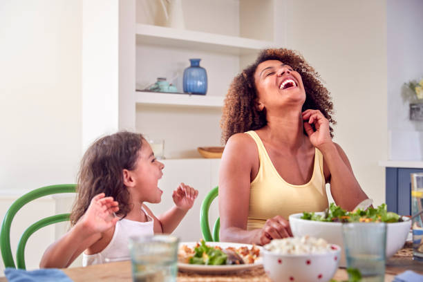 Mother And Daughter Sitting Around Table At Home Enjoying Eating Family Meal Together stock photo