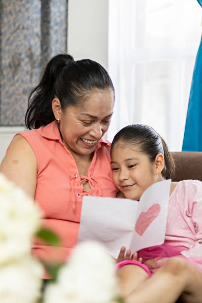 mother and daughter smiling and giving each other a hug while reading a mother's day greeting card mother and daughter smiling and giving each other a hug while reading a mother's day greeting card hot mexican girls stock pictures, royalty-free photos & images