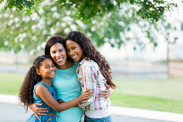 Mother and daughters hugging tightly and smiling at camera A latin mother and her two daughters embracing tightly and smiling at the camera in a horizontal waist up shot outdoors. mexican teenage girls stock pictures, royalty-free photos & images