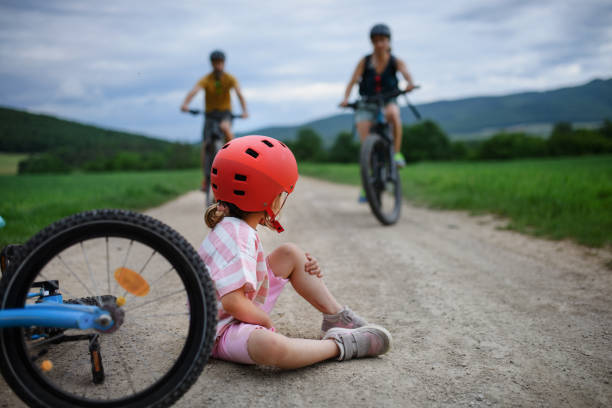 Mother and father rushing to help their little daughter after falling off bicycle outdoors stock photo