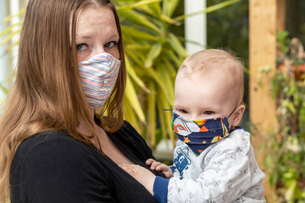 Mother and her baby in reusable protective face mask stock photo