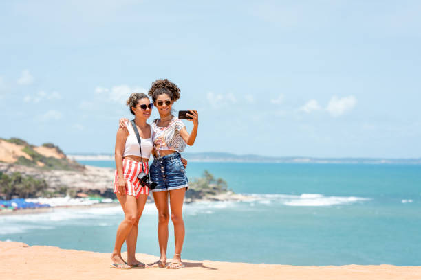 Mother and her teenager daughter taking a self at the beach Mom and her teenager daughter taking a self at the beach in a sunny day during their vacations. brasil stock pictures, royalty-free photos & images