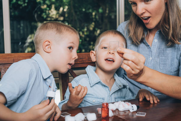 Mother and her two little sons doing the experimental laboratory activity together with colored water and pieces of glass. stock photo