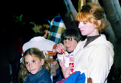 Vintage photo featuring a mother and her children during a family trip, standing in the crowd outdoors and eating chips. Vintage photo of the eighties of the 20th century.