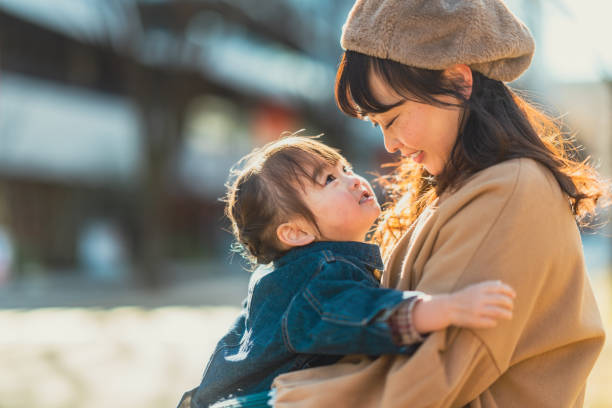 Mother and small girl sitting at bench and enjoying spending time together in city in winter on sunny warm day stock photo