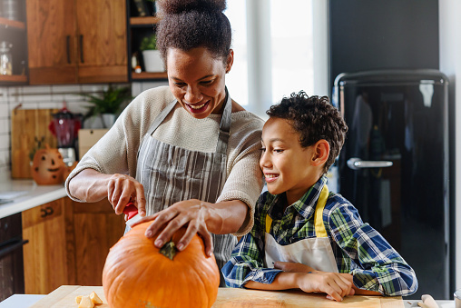 Mother and son carving pumpkin for Halloween holiday. African american ethnicity family.