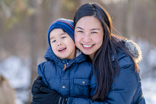 Asian mother and her adorable 3 year old son enjoying quality time outside in the snow during the winter months.