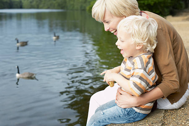 Photo of Mother and son feeding ducks in pond