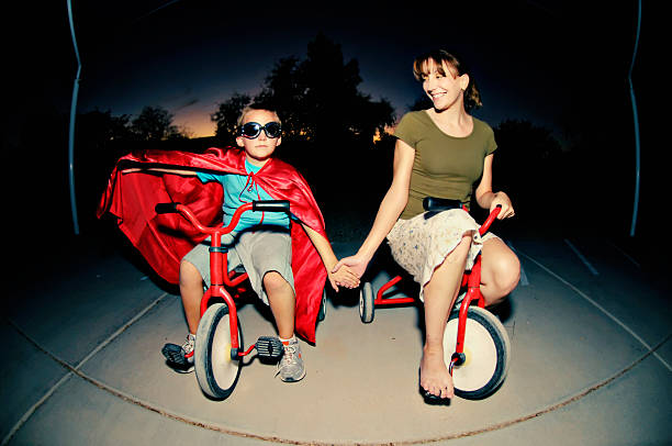 Mother and son in cape riding tricycles in the dark stock photo