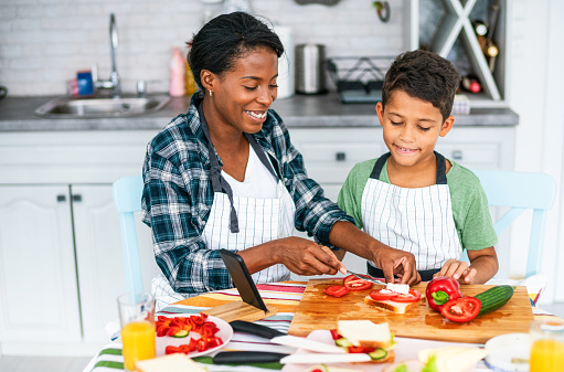 Young african-american mother and her cute son preparing healthy and tasty sandwiches together in the kitchen.