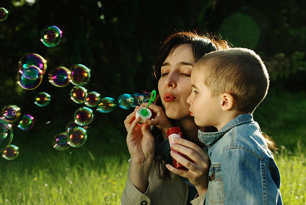 Mother and son making soap bubbles outdoors stock photo