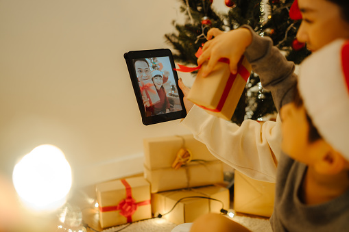 Happy family with a child is celebrating Christmas with their friends on video call using digital tablet