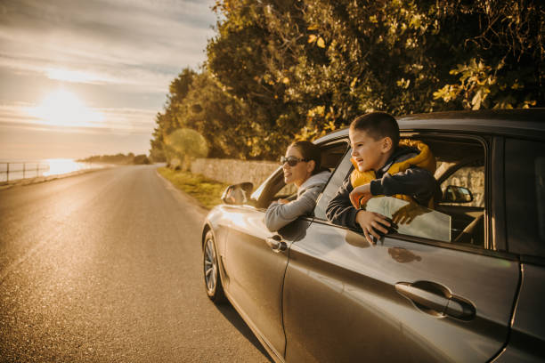 Mother and son sitting in car on road and enjoying the sea view during sunset stock photo