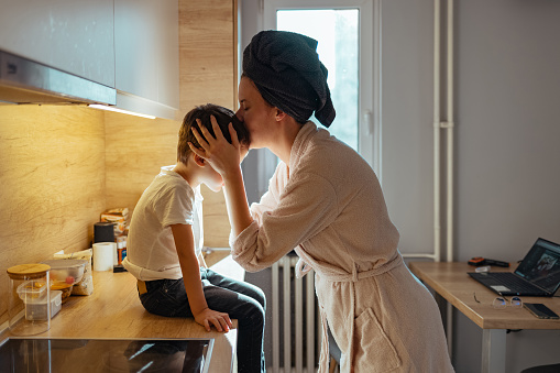Boy being kissed by his mother while sitting on kitchen counter during the day.