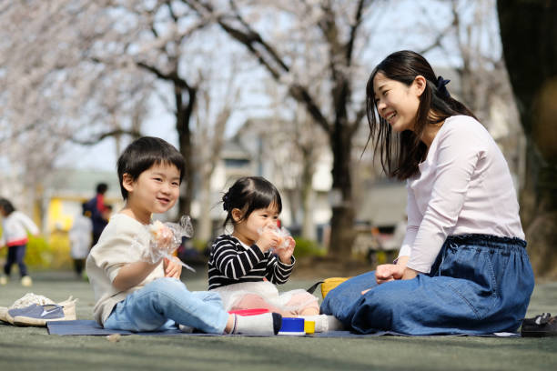 桜の木の下で昼食を食べるお母さんと二人の子供 - 花見 ストックフォトと画像