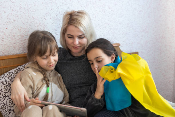 mother and two daughters are reading with the flag of ukraine in bed stock photo