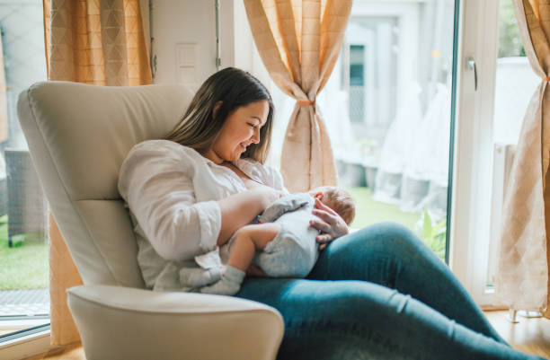 Mother breastfeeds and plays with her newborn baby stock photo