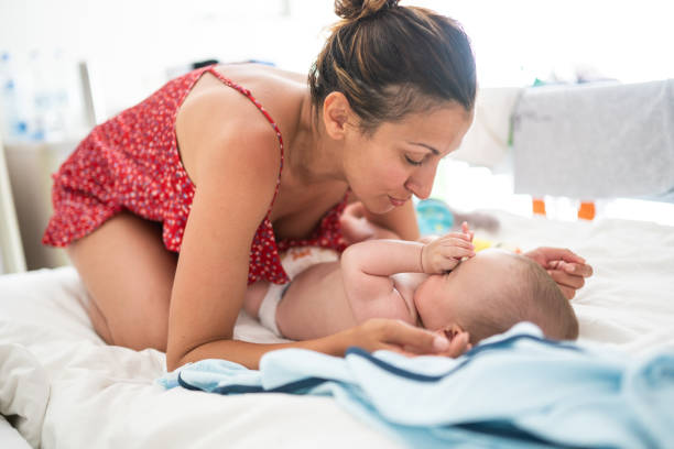 Mother changing diaper to sleepy baby boy Beautiful woman changing diaper to adorable  baby,cute boy laying on bed in the bedroom, on sunny morning tickling beautiful women pictures stock pictures, royalty-free photos & images