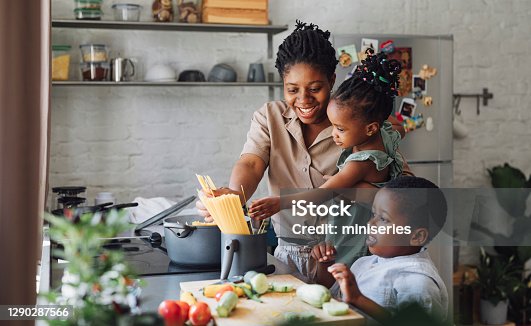 istock Mother, Daughter and Son Preparing Spaghetti and Vegetables for Lunch over a Cutting Board 1290287566