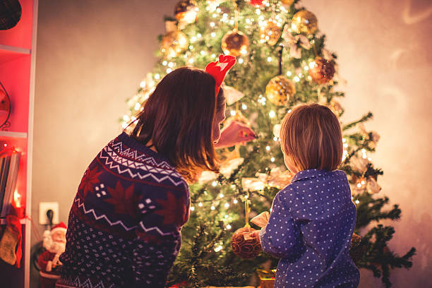 mother decorating christmas tree with her son - vrouw kerstboom versieren stockfoto's en -beelden