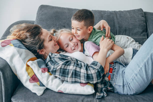 Mother enjoying time with kids Happy young mother playing on the sofa with her cute son and daughter. tickling beautiful women pictures stock pictures, royalty-free photos & images