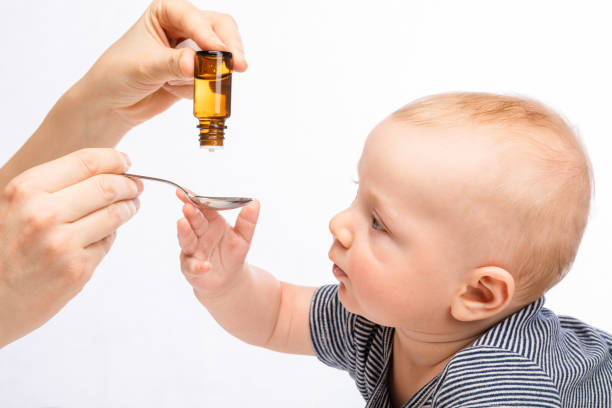 Mother feeding baby boy with liquid medicine stock photo