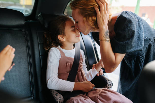 Mother giving her eight year old daughter a kiss. She's sitting on a back seat. stock photo