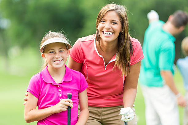 Mother have fun while playing golf together Pretty mid adult woman and her preteen daughter are playing golf with their family on a sunny day at local golf course. The girl's father and her brother are in the background. They are both wearing golf shirts. irish women stock pictures, royalty-free photos & images