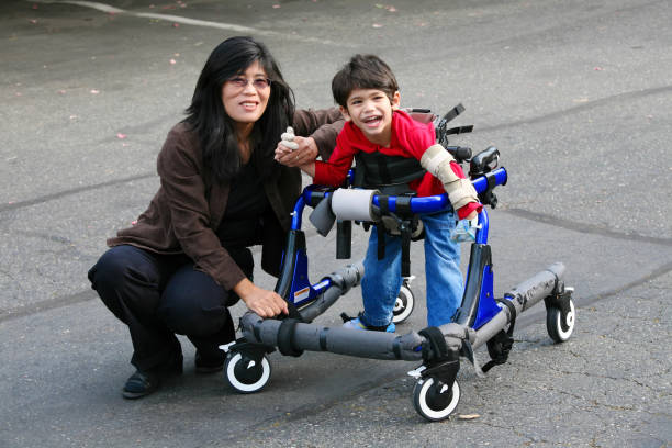 Mother helping disabled son walk in walker outdoors stock photo