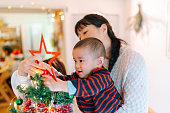 自宅でクリスマスツリーを飾って彼女の小さな息子を助ける母
