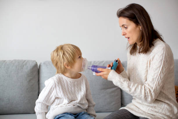 Mother, helping little toddler child with inhaler with spacer stock photo