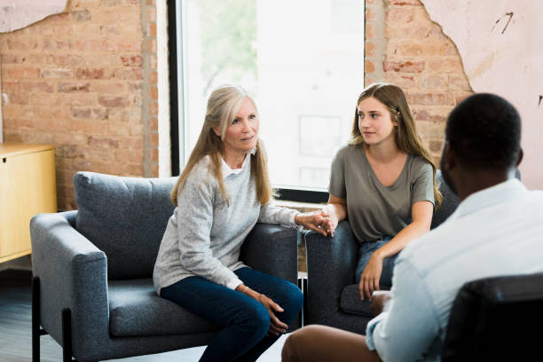 Mother holding daughter's hand talks to unrecognizable male therapist stock photo