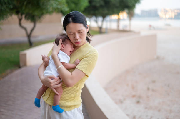 Mother holding newborn baby boy by the seaside on the beach at sunset Asian woman holding her newborn baby boy by the seaside on the beach at sunset. Mother and son on the seaside, new life and family love abstract  soothe crying baby stock pictures, royalty-free photos & images