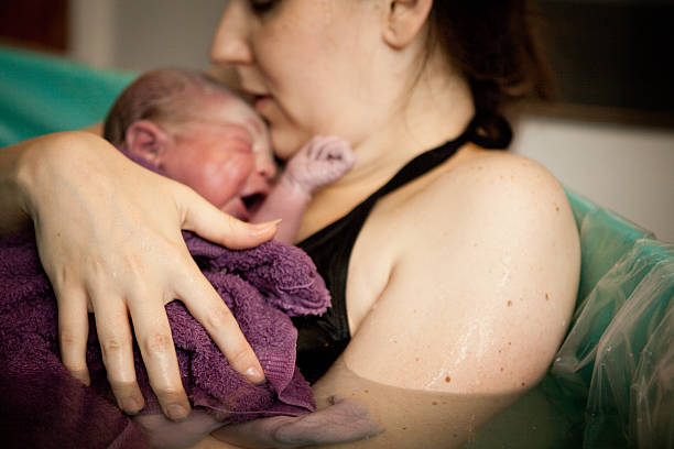 Mother Holding Newborn in Birthing Tub After Home Water Birth Color photo of a loving mother holding her newborn baby son in the water of a birthing tub immediately after a water birth at home. childbirth stock pictures, royalty-free photos & images