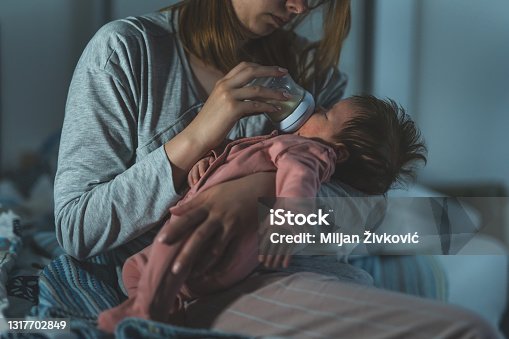 istock Mother holds her two moths old baby taking care of her at home - Caucasian woman with her newborn child bottle feeding milk on lap at night - Affectionate and bonding childhood and motherhood concept 1317702849