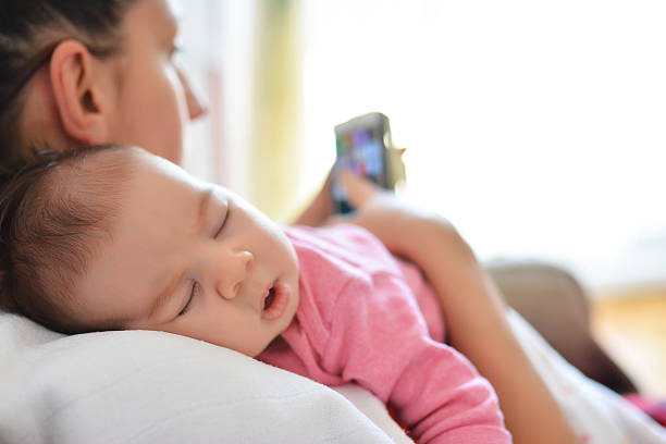 Mother In Bed With Baby Daughter Checking Mobile Phone stock photo