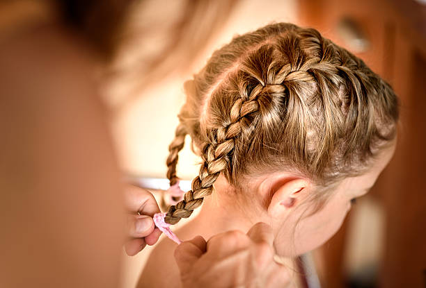 Mother is making of braids on little daughter's head. stock photo