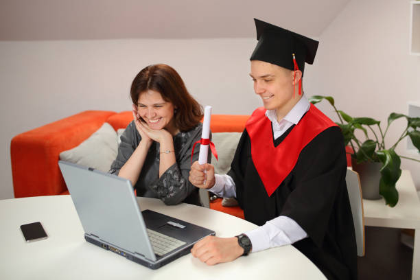 Mother looks at Laptop screen with happy students in graduation gown and a square cap during Virtual graduation ceremony Mother looks at Laptop screen with happy students in graduation gown and a square cap while Virtual graduation ceremony and convocation phd programs online stock pictures, royalty-free photos & images