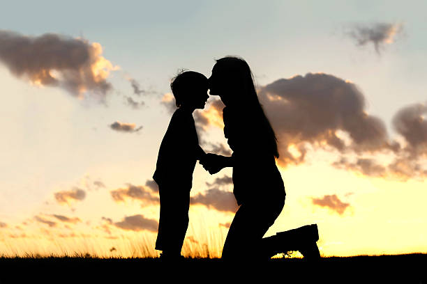 Mother Lovingly Kissing Little Child at Sunset stock photo
