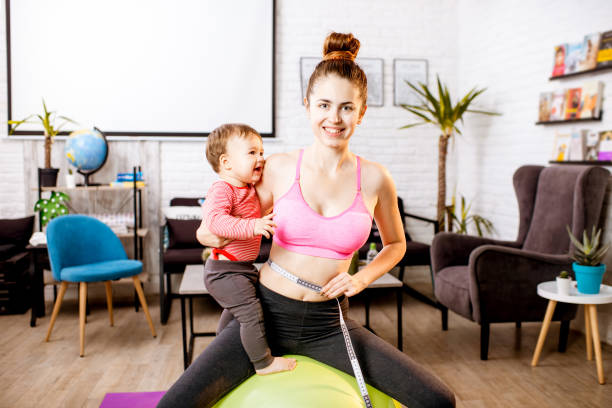Mother measuring her waist Young mother in sportswear measuring her waist worried about her weight after the child birth sitting with her baby son during the exercise belly fat  pregnancy stock pictures, royalty-free photos & images