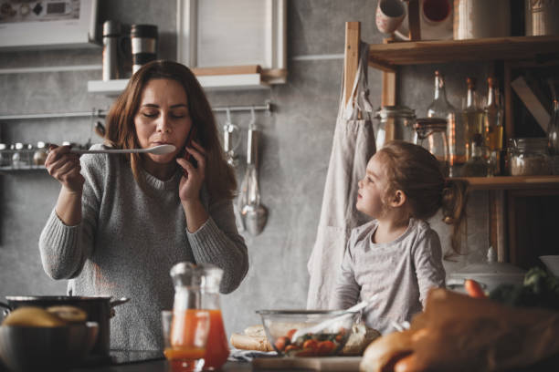 Mother on the phone, cooking Mother and daughter cooking together, woman talking on the phone. tasting stock pictures, royalty-free photos & images