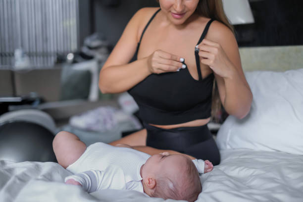 Mother Preparing To Breastfeed Her Baby Close-up shot of a mixed race mother unhooking the clasp on her breastfeeding black singlet bra while watching her newborn baby girl lying on the bed. indonesian girl stock pictures, royalty-free photos & images