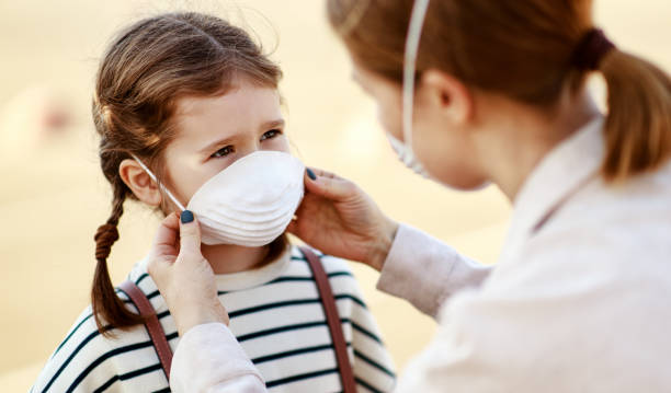 Mother putting on medical mask on daughter From above adult woman putting on medical mask of little girl while standing on city street during coronavirus pandemic contamination photos stock pictures, royalty-free photos & images