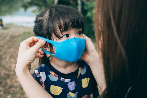 母親在公園裡為小女兒戴上手術面罩，防止感冒、流感和病毒的傳播圖像檔