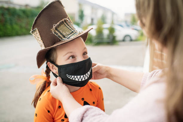 mãe colocando máscara facial protetora em seu filho durante pandemia covid-19 no halloween - máscara covid - fotografias e filmes do acervo