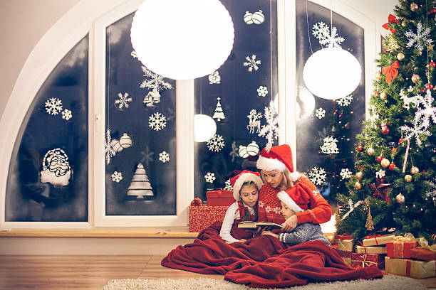 Mother reading Christmas story to her children Mother reading Christmas story to her children. christmas story telling stock pictures, royalty-free photos & images