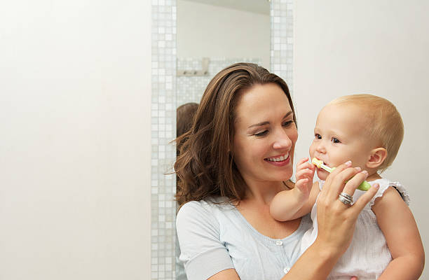 Mother teaching baby how to brush teeth with toothbrush stock photo